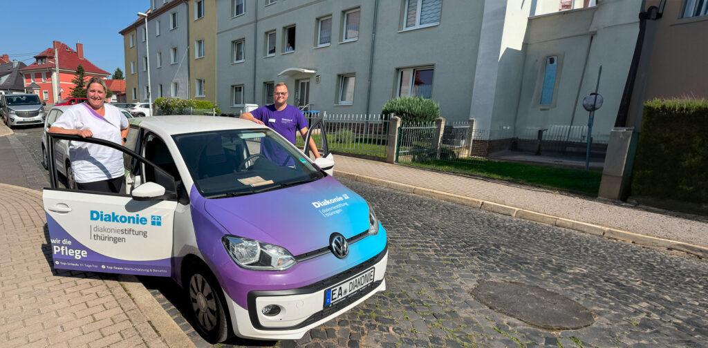 Mitarbeiterin und Mitarbeiter des Diakonie Pflegedienstes Eisenach stehen an ihrem Pflegedienstauto