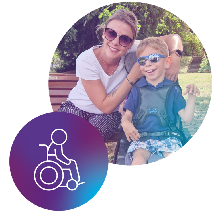 Eine Frau sitzt lächelnd neben einem lachenden Kind mit Beeinträchtigung