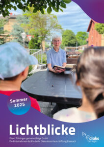 Seniorin sitzt am Gartentisch zwei Menschen gegenüber und liest vor