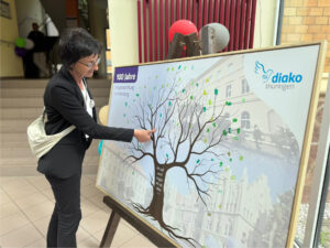 Elke Slowik, Vorstand Diako Thüringen, füllt einen symbolischen Ausdruck eines Baums mittels grünem Fingerabdruck mit Laub