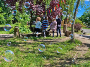 Evang. Kindergarten Schleiz, vier Kinder im Garte mit Seifenblasen