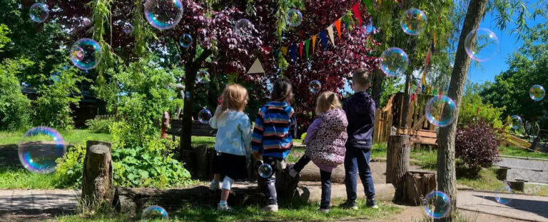 Evangelischer Kindergarten Schleiz, drei Kinder im Garten, umgebe von Seifenblaaen