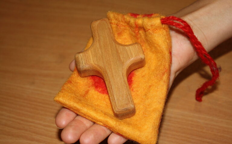 Holzkreuz auf Filzsäckchen wird in einer geöffneten Hand gehalten