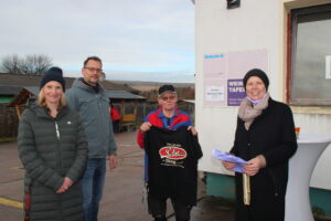 Sozialkontor Johannes Falk, Tafel Weimar, vier Personen am Hausschild, eine Frau zeigt ein T-shirt