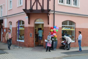 ThINKA Bad Lobenstein und Pößneck, Eingang zum Diakonieladen Bad Lobenstein mit Menschen und Luftballons