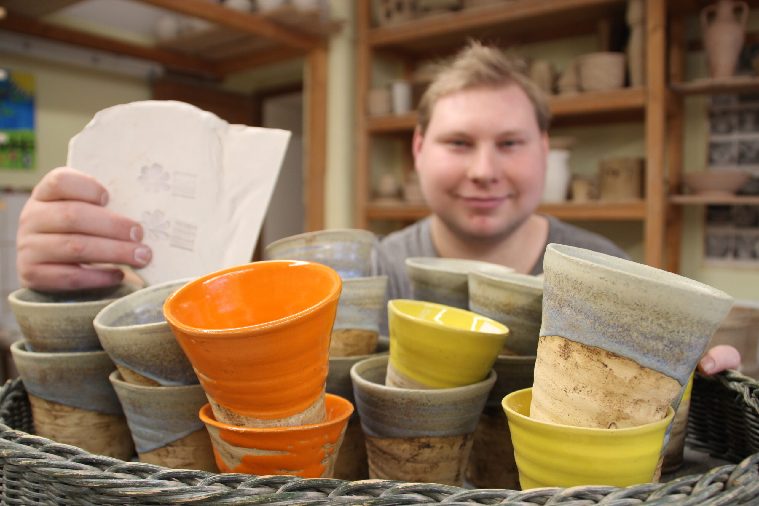 Töpferei Werkstätten Christopheruhof Altengesees, junger Mann vor farbigen Saftbechern aus Ton
