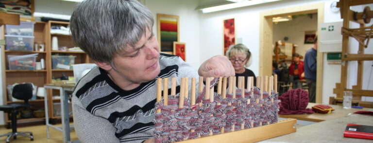 Weberei der Werkstätten Christopherushof in Altengesees, junge Frau webt ein Sitzkissen aus Stoffresten