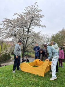vier Jugendliche tragen eine Holzbank