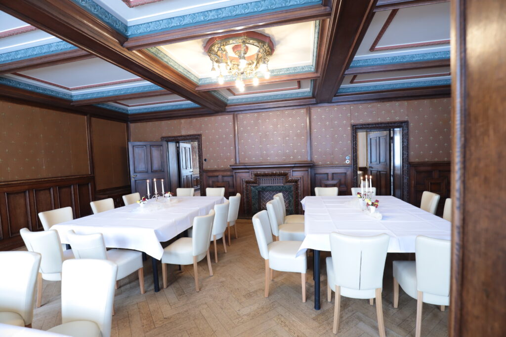 Landgut Holzdorf Blick in das Lederzimmer, Tafeln mit weißen Tischdecken und weißen Stühlen