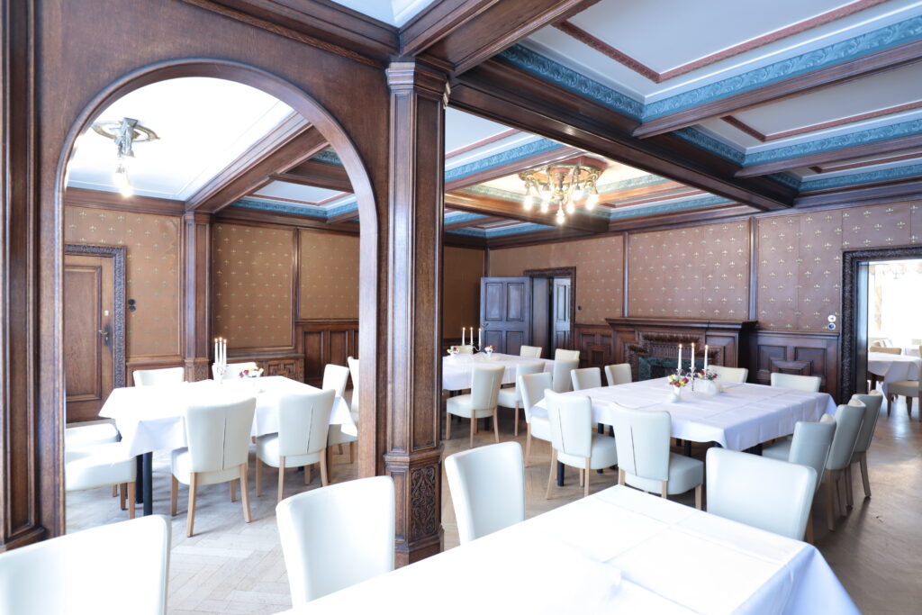 Landgut Holzdorf Blick in das Lederzimmer, Tafeln mit weißen Tischdecken und weißen Stühlen