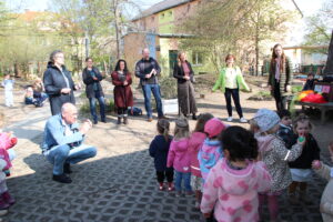 Senfkornspende-Übergabe, Erwachsene und Kinder im Garten 