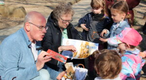 Senfkornspende-Übergabe, Mann kniet und wird von Kindern umringt